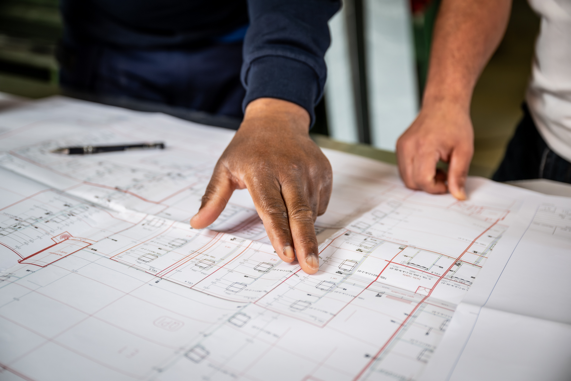 Hand wijst naar bouwtekening op tafel.