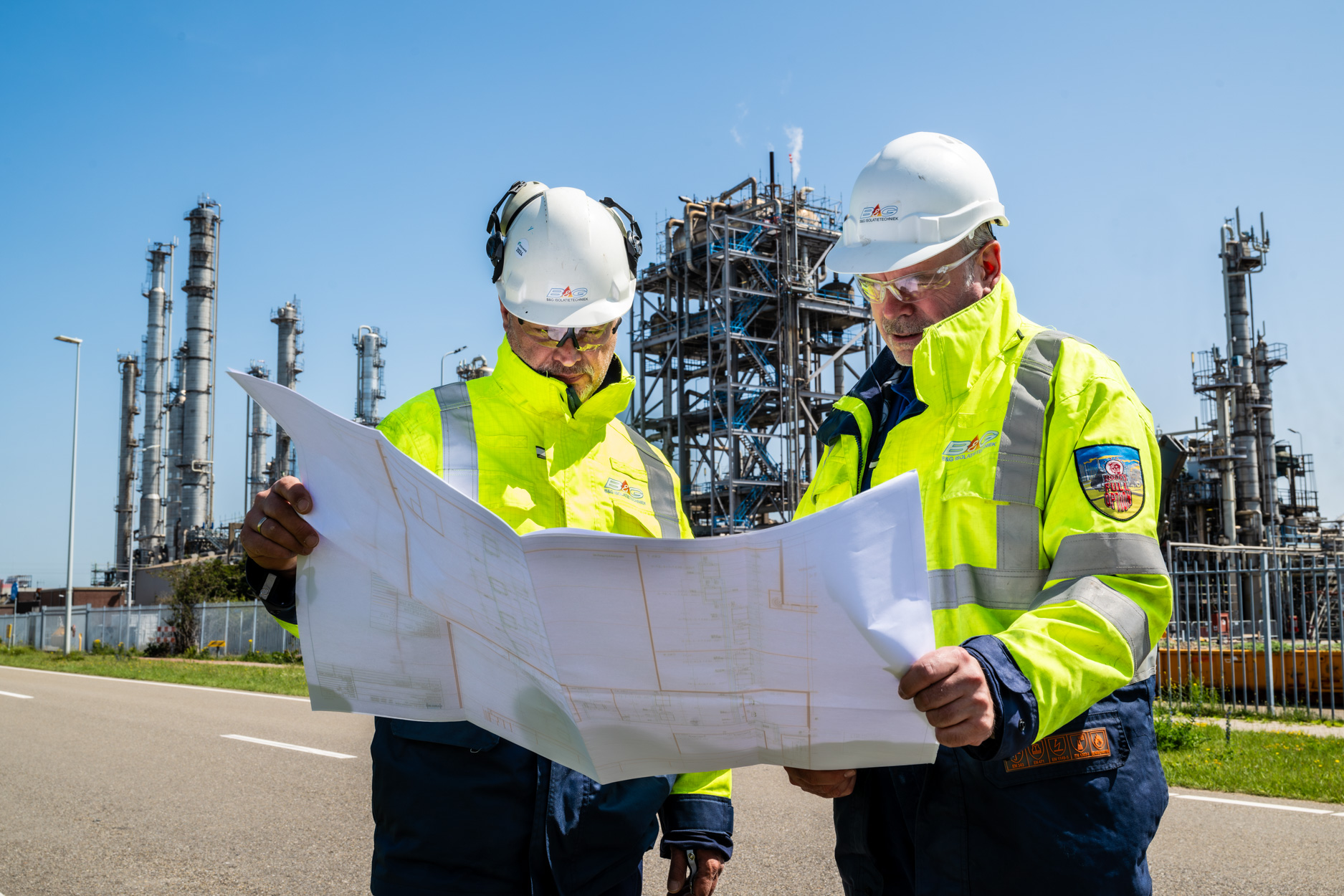 Twee mannen in veiligheidskleding bekijken bouwplannen bij fabriek.