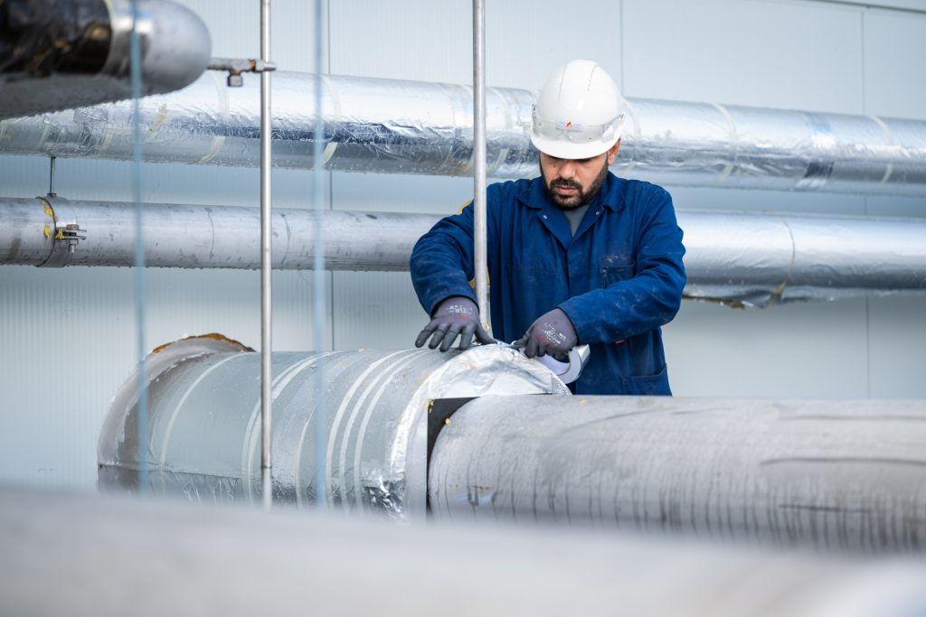 Technicus werkt aan geïsoleerde leidingen in fabriekshal.