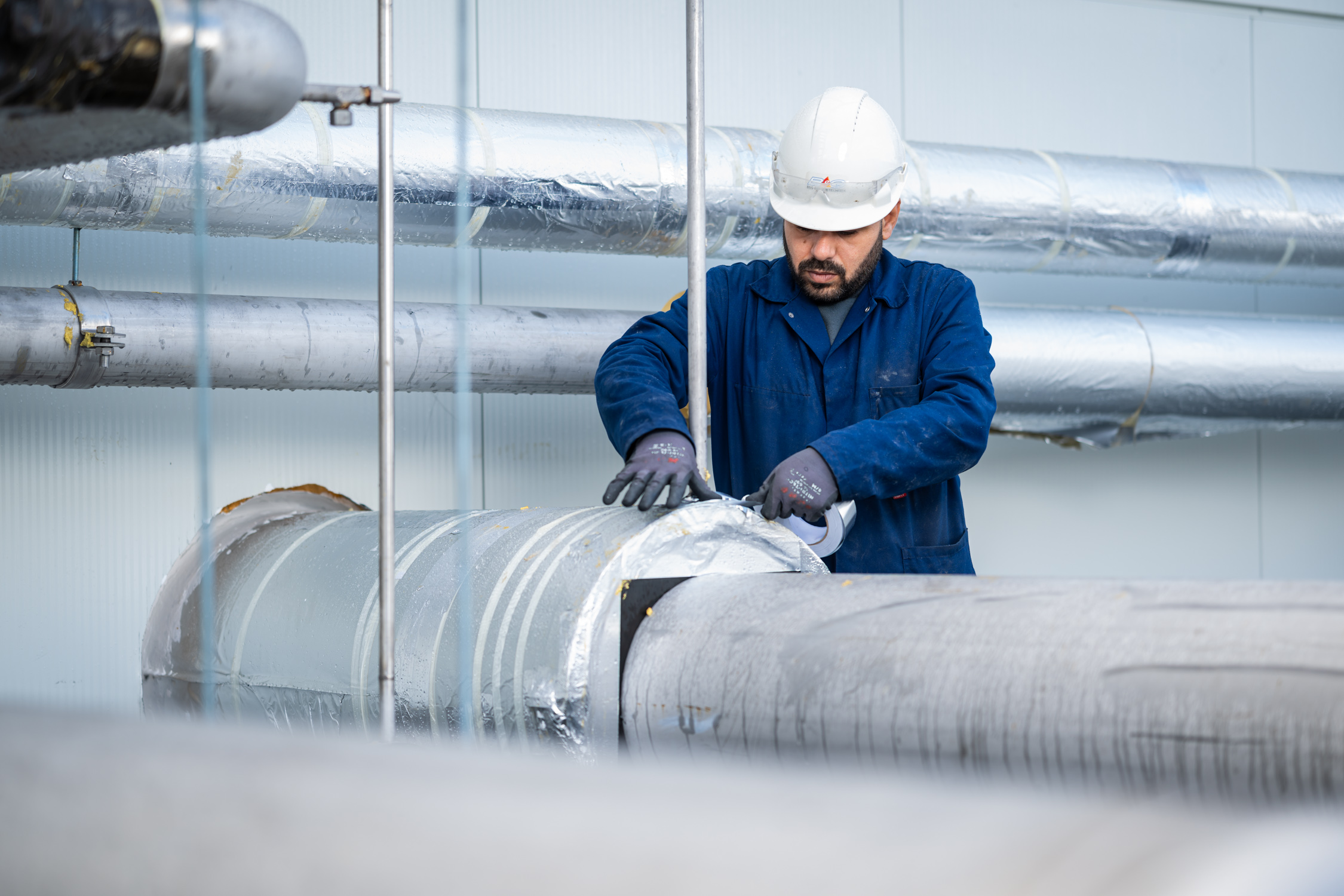 Technicus werkt aan geïsoleerde leidingen in fabriekshal.