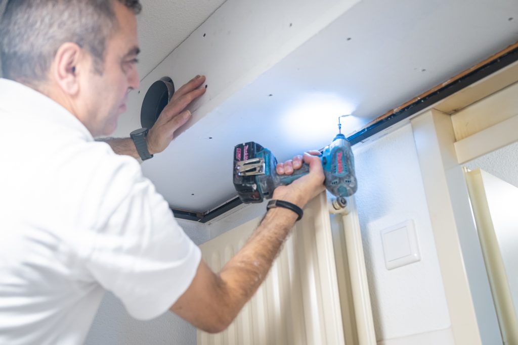 Man boort gat in plafond met boormachine.