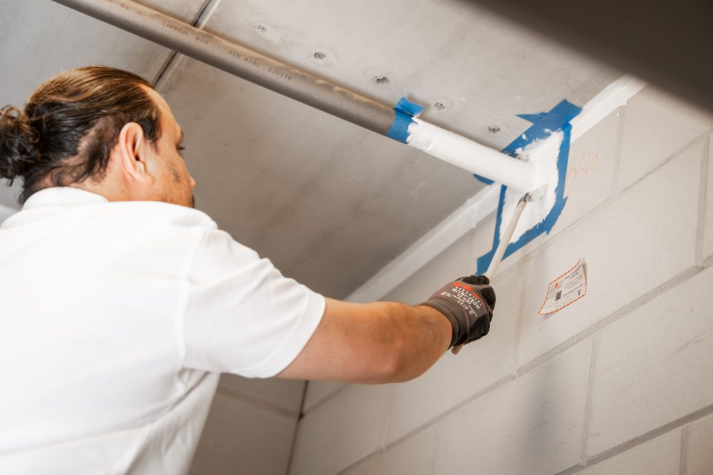Persoon schildert buis wit op muur.
