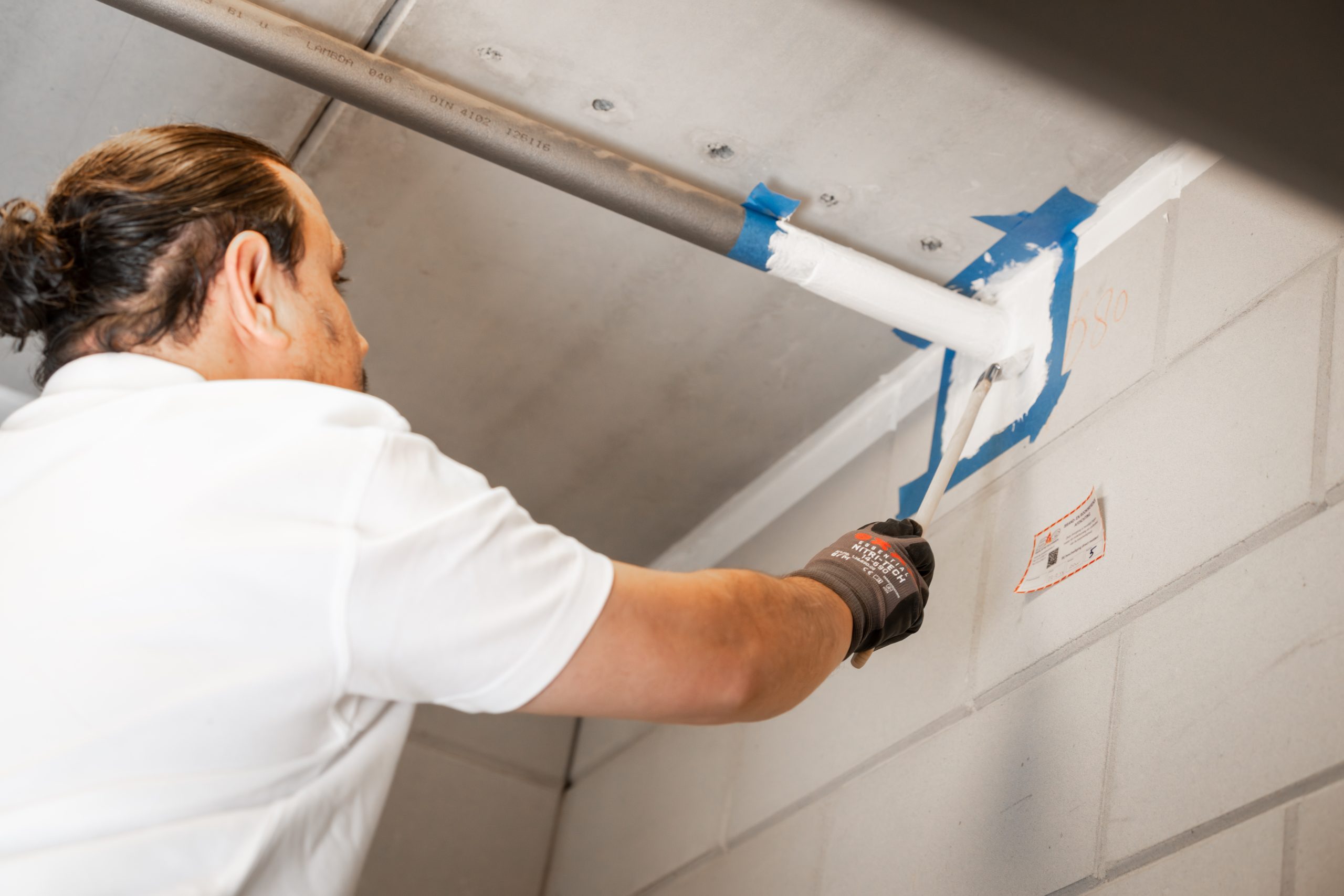 Persoon schildert buis wit op muur.